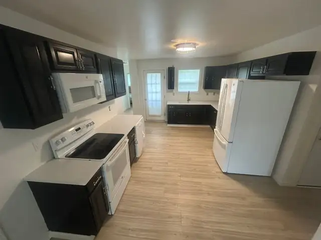 Kitchen with dark espresso cabinets, white countertops, white appliances and light wood-look plank flooring