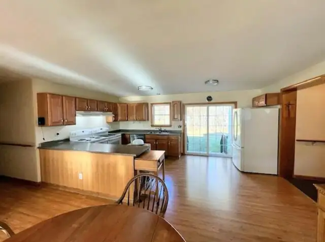 Large kitchen with wood cabinets, a peninsula with dark counters and wood-look floor opening to a deck door