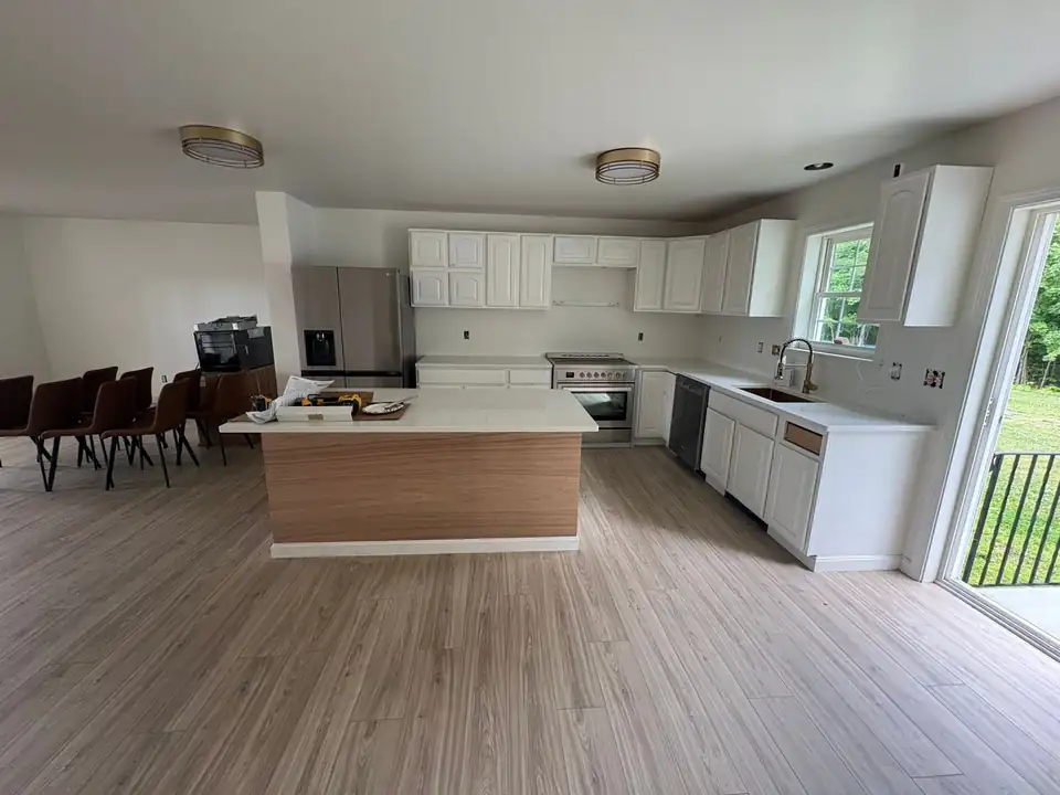 Kitchen remodeling in Waterville: white cabinets, island with white top and wood panel base, and new light wood-look plank floor