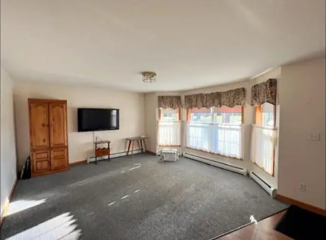 Finished room with bay windows, gray carpet, wall-mounted TV and wooden armoire